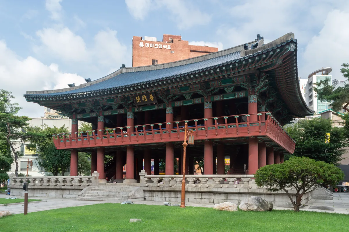 Bosingak in Seoul - A compact two-storey wooden pavilion with a blue-tiled hipped roof, standing alone on an island of...
