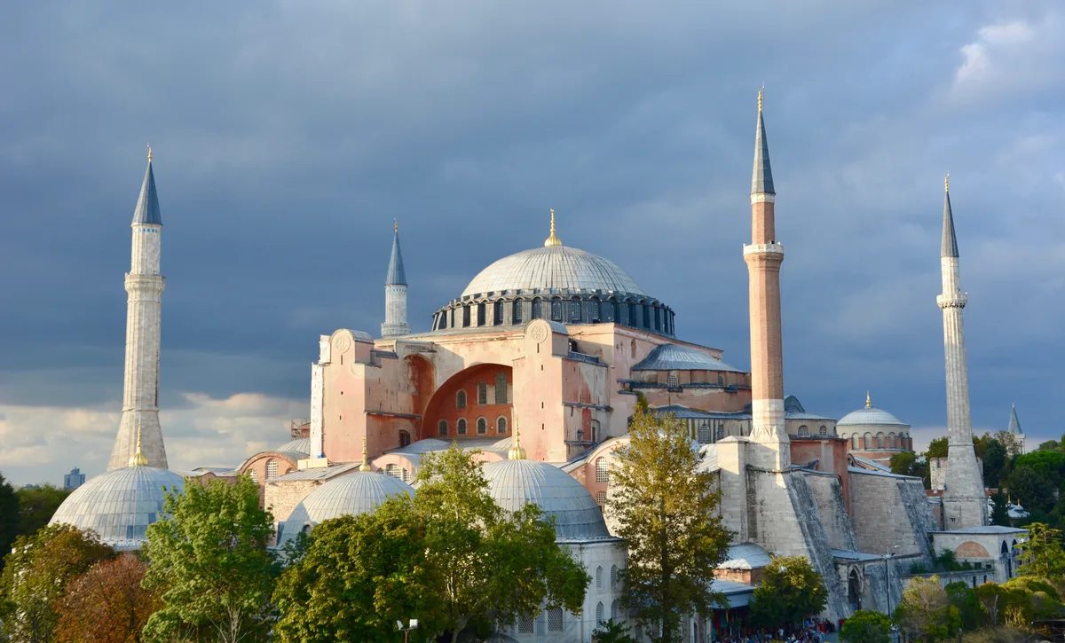 Hagia Sophia in Istanbul - A massive terracotta-colored structure defined by its towering dome, flanked by four soaring...