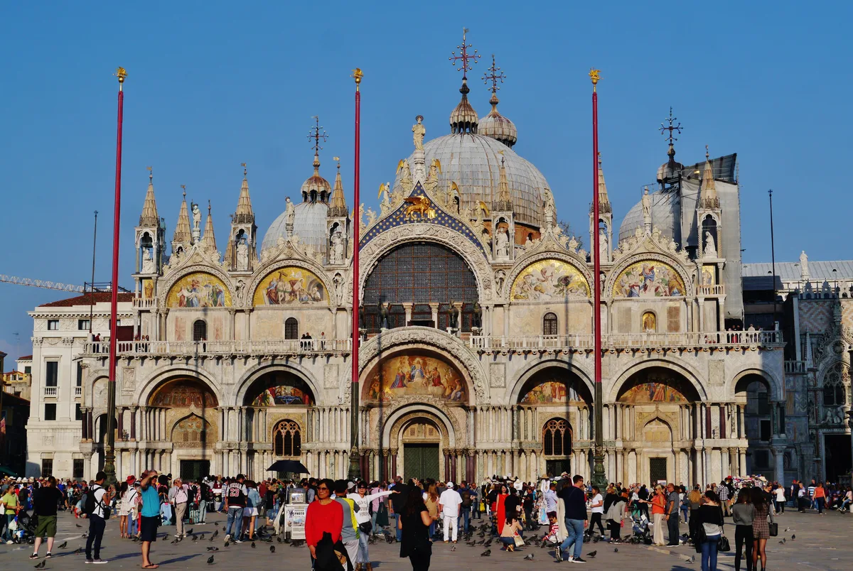 St. Mark's Basilica in Venice - Five grey-white domes rise above a facade crowded with columns, gold mosaics, and four...