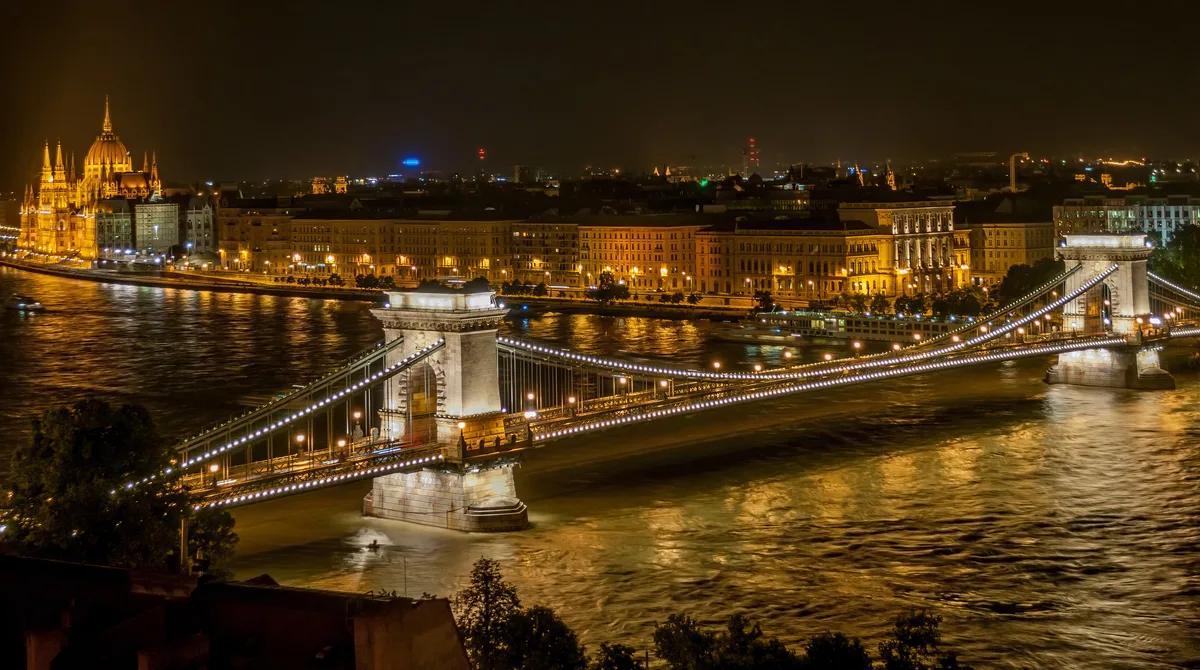 Szechenyi Chain Bridge in Budapest - A green iron chain suspension bridge stretching across the Danube, its tall stone...